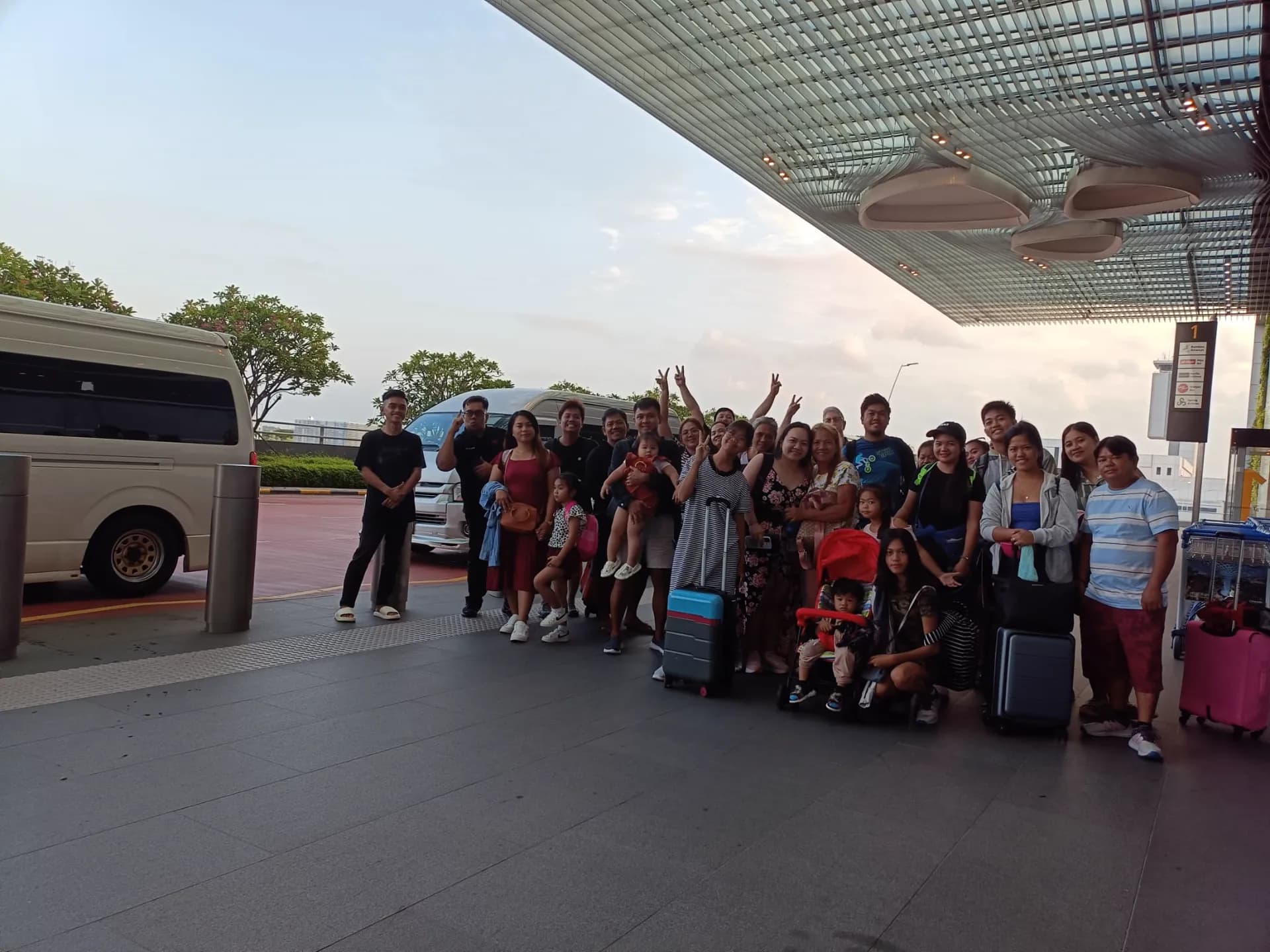 A large multi-generational family with luggage at the Changi Airport kerb beside two Platinum Maxi Cab vehicles